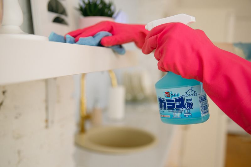 Hands in pink gloves wiping a counter with a cloth and a spray bottle
